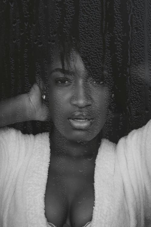 Free Artistic grayscale portrait of a young woman behind a rain-covered window, expressing a contemplative mood. Stock Photo