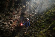 A Man in Blue Jacket Holding a Flare While Standing on the Mossy Rocks in the Cave