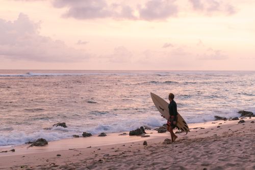 Free A serene scene of a surfer holding a board on the beach during a beautiful sunset. Stock Photo
