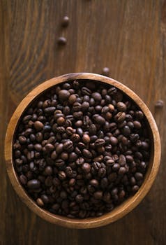 A top view of roasted coffee beans in a wooden bowl on a rustic table surface.