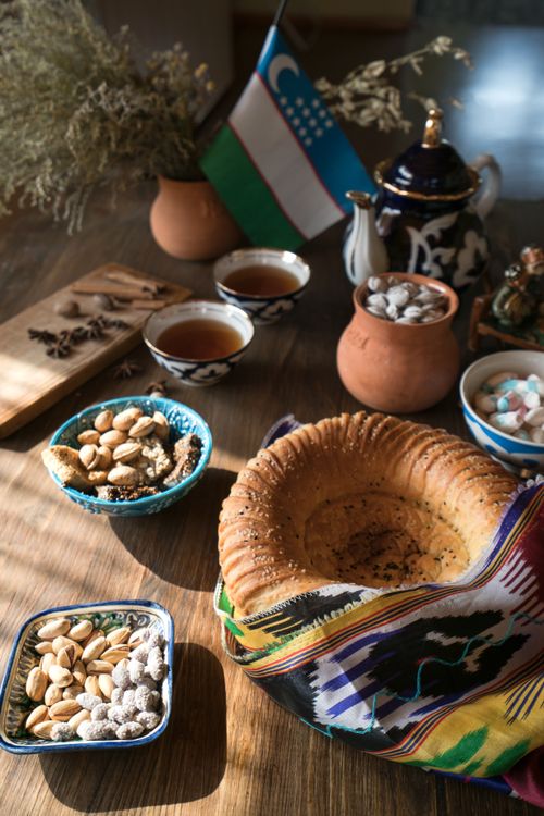Free A spread of Uzbek bread, nuts, and tea on a wooden table with cultural elements. Stock Photo