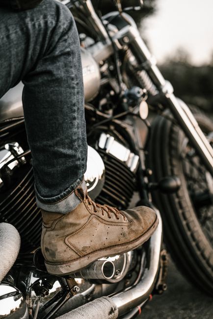 Person wearing boots sitting on a motorcycle, highlighting the engine details.