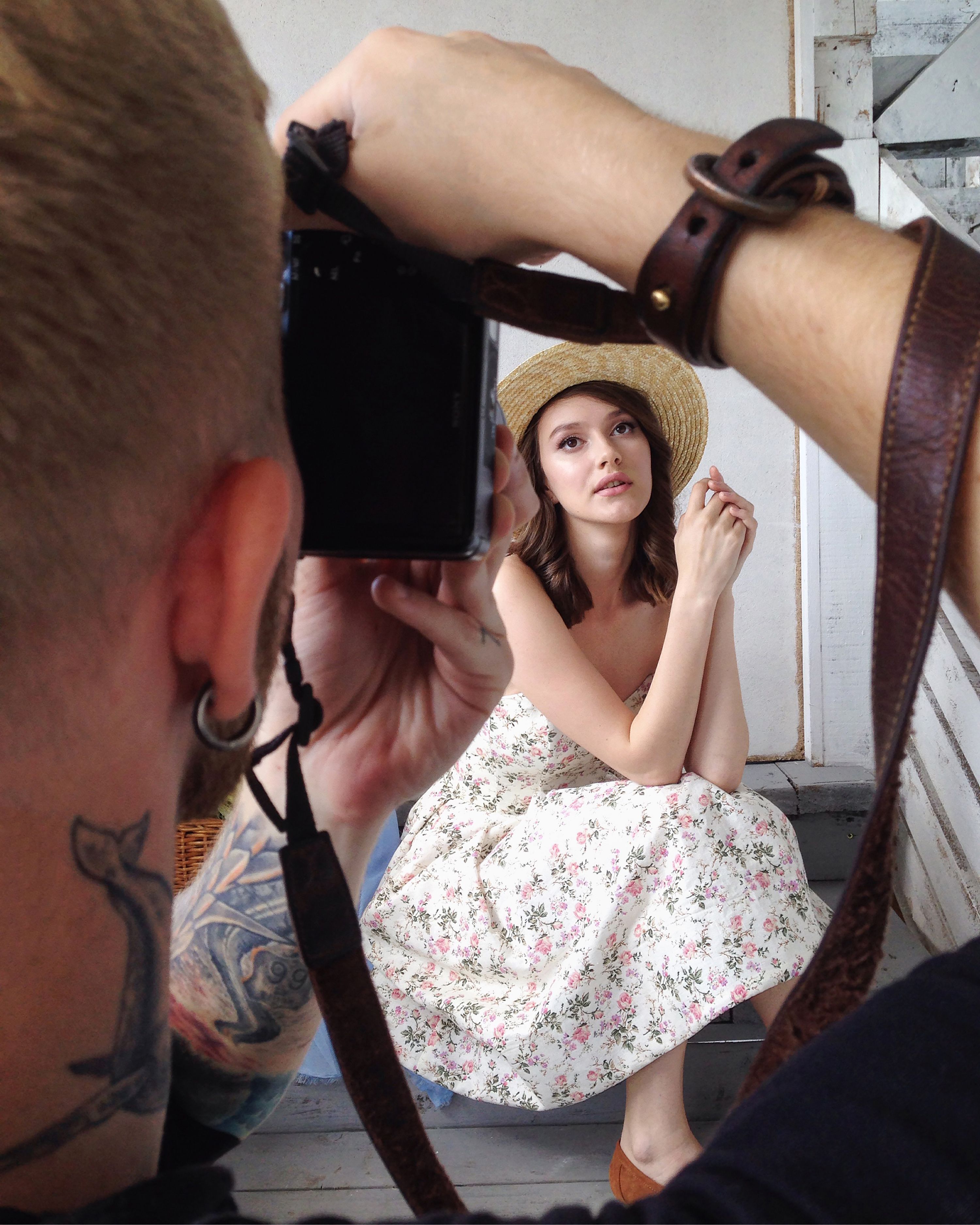 Photographer capturing a woman in floral dress and straw hat on stairs.