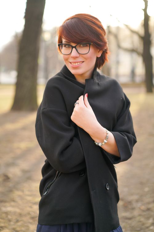 Free A young woman with glasses and dyed hair smiles in a public park during autumn. Stock Photo