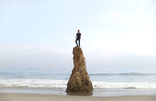 Man Standing on Top of Rock on Beach