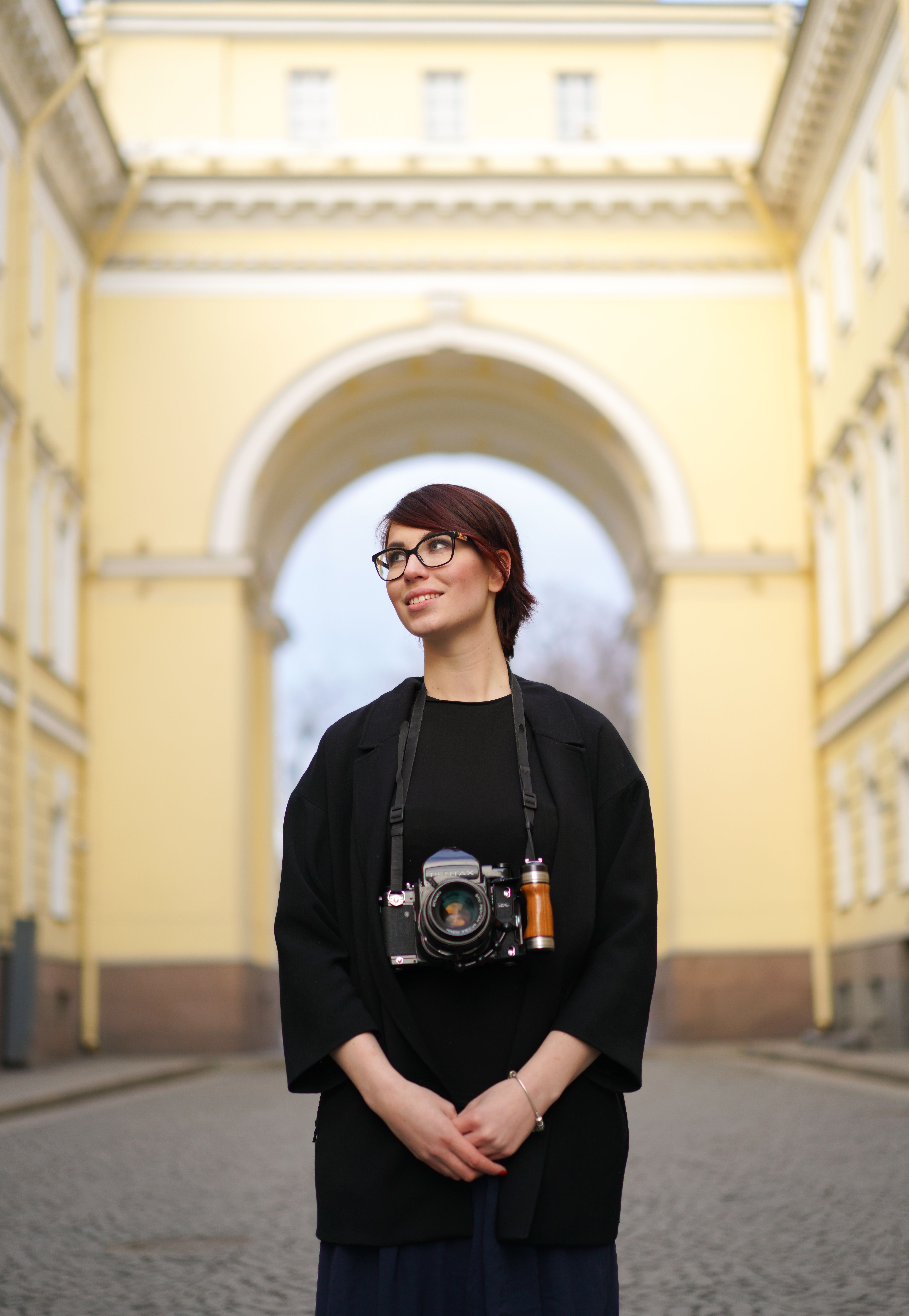 Smiling woman with a camera posing in an urban archway setting.