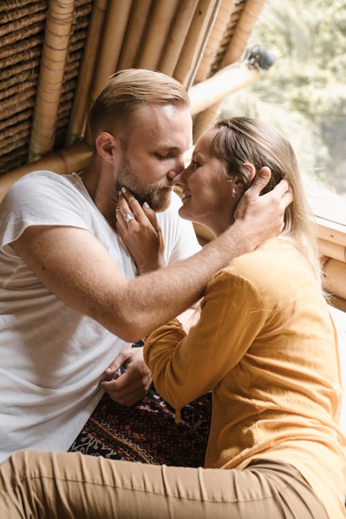 Man in White Crew Neck T-shirt Kissing Woman in Brown Shirt