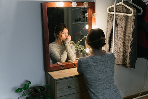 Free Woman in Gray Sweater Sitting in Front of a Mirror Stock Photo
