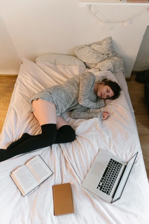 Free Young woman lying in bed with a laptop and books, enjoying a quiet moment. Stock Photo