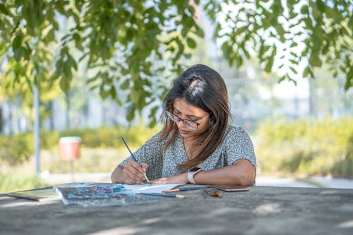 Focused young ethnic lady drawing in park on sunny day