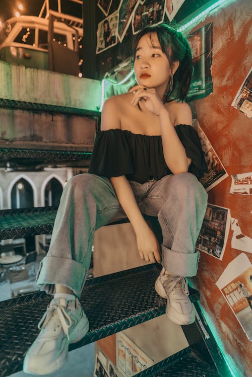 Stylish young ethnic lady sitting on staircase in modern cafe