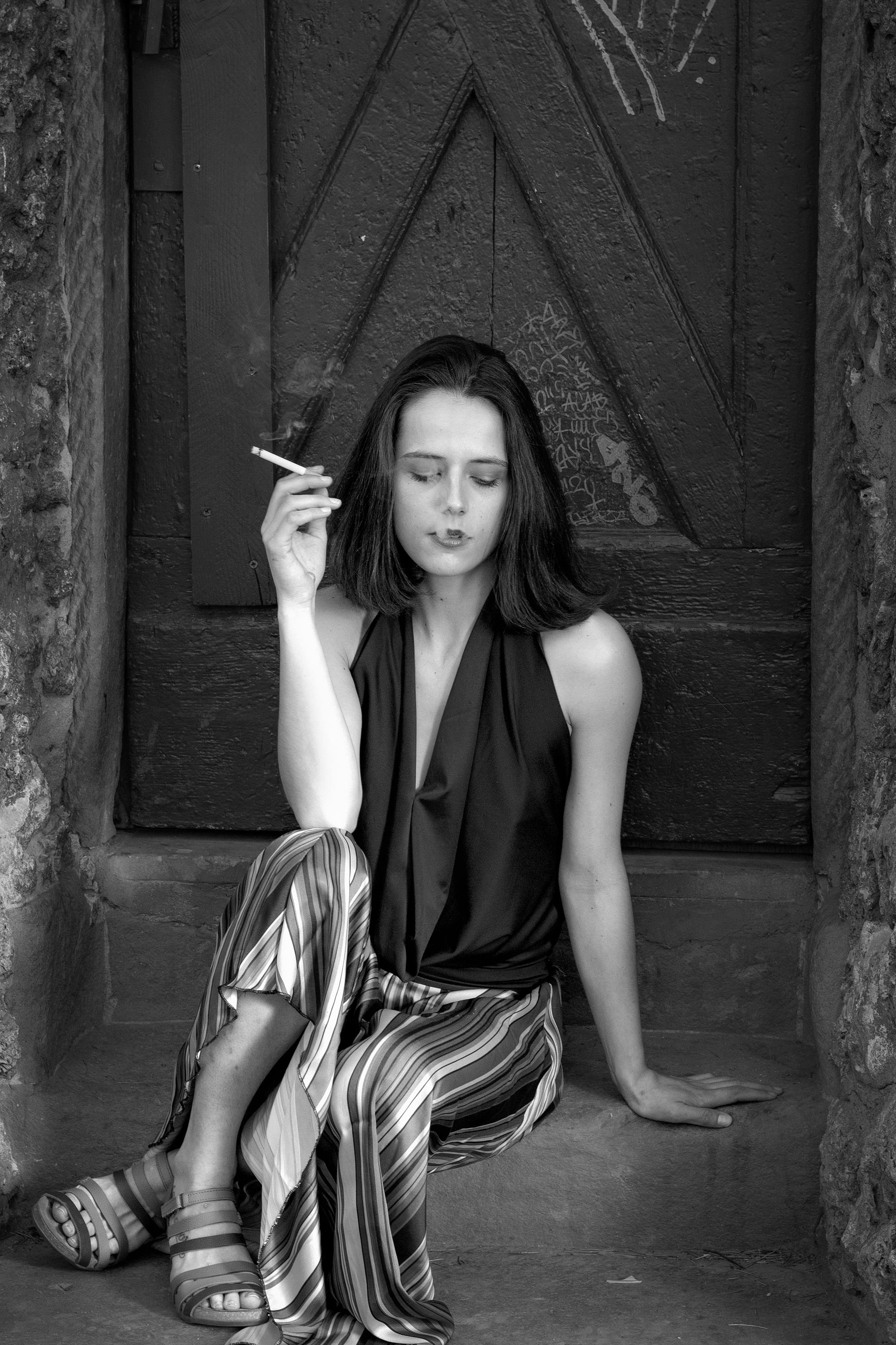 thoughtful young lady smoking cigarette on steps of aged house