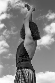 Side view of black and white gorgeous young female in elegant dress dancing gracefully against cloudy sky