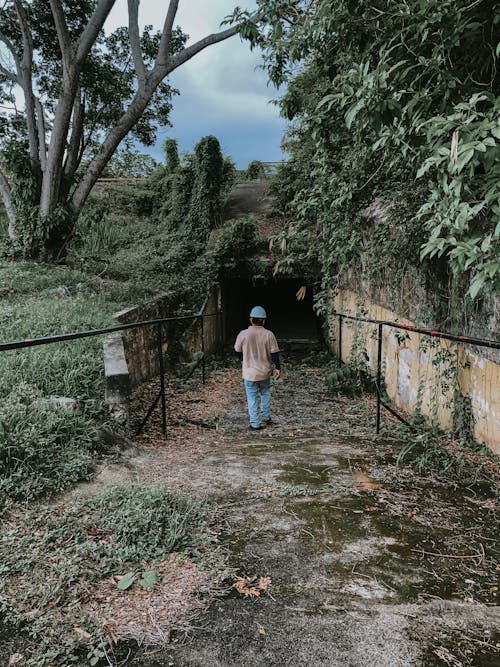Man walking down path towards dark underground passage