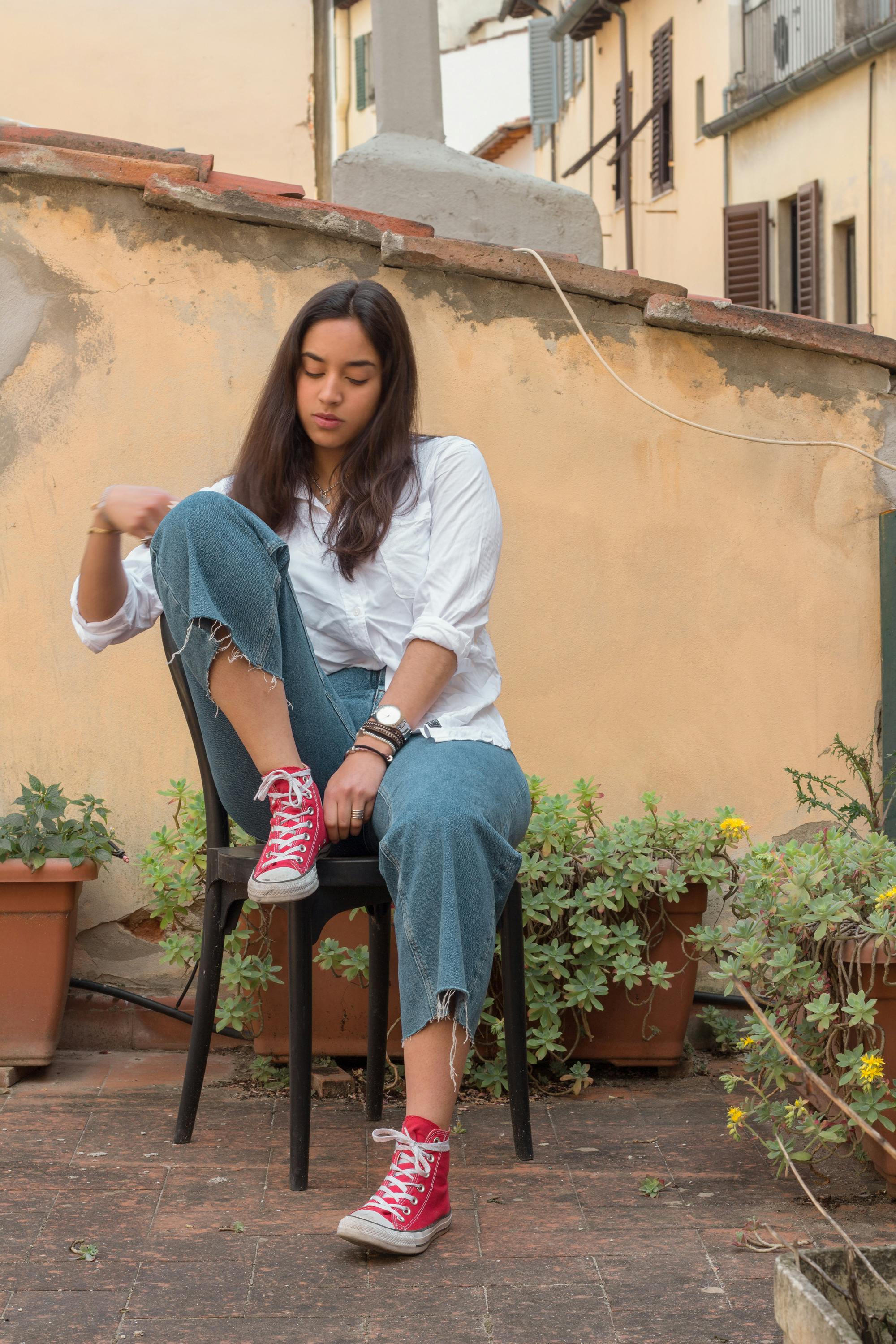 一个穿着休闲服的严肃女人，正坐在椅子上，若有所思地低头向下看，这是一个低角度的全身镜头