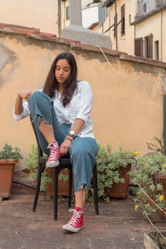 一个穿着休闲服的严肃女人，正坐在椅子上，若有所思地低头向下看，这是一个低角度的全身镜头