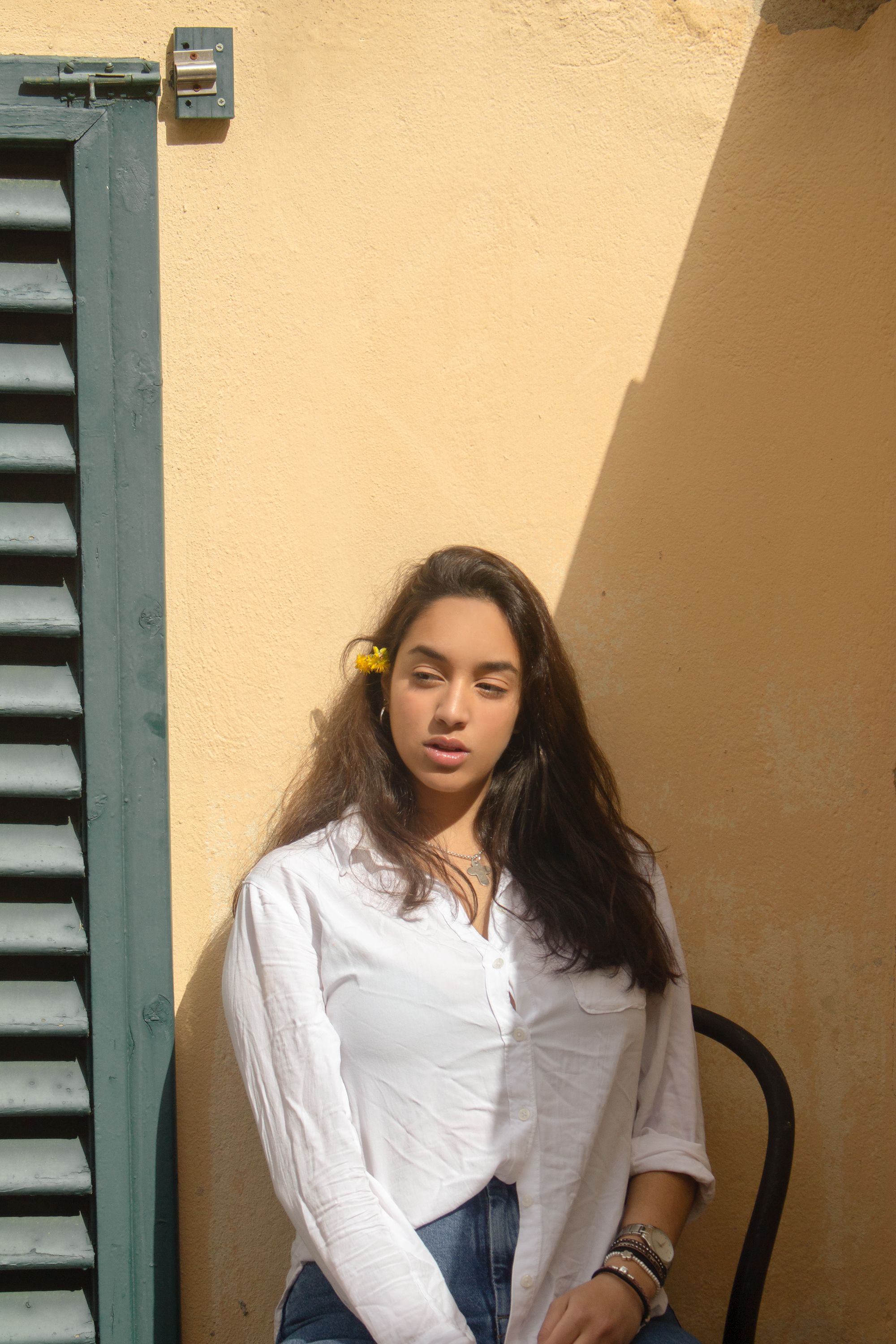 Portrait of a brunette woman in a white shirt, with natural light creating shadows against a wall.
