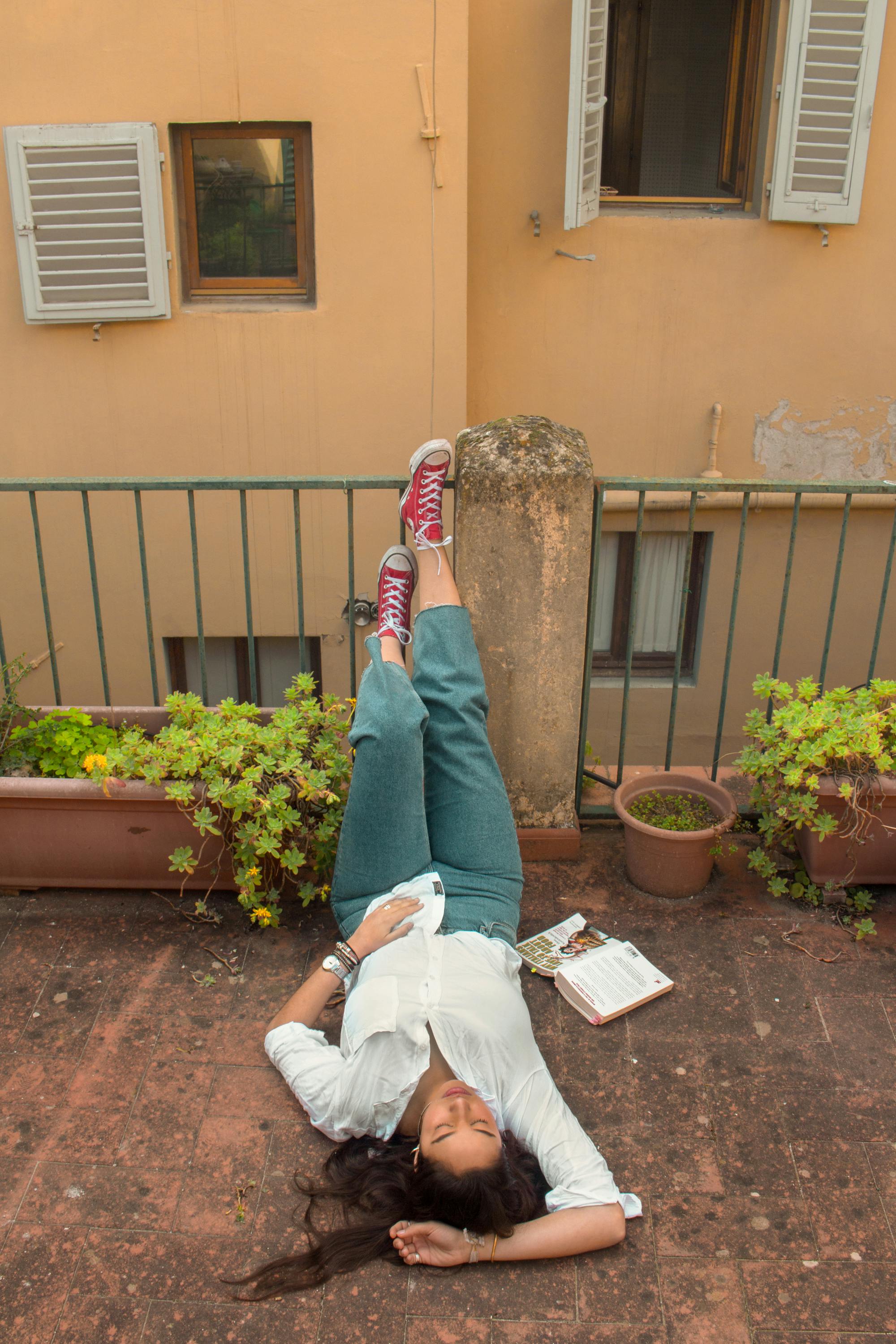 A woman relaxes on a balcony, lying down with a book beside her, embodying leisure and tranquility.