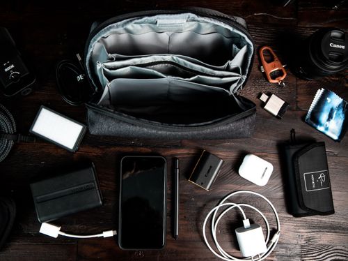Free Top view of arranged tools including smartphone camera lens charging flash drives wireless headphones in case placed near bag Stock Photo