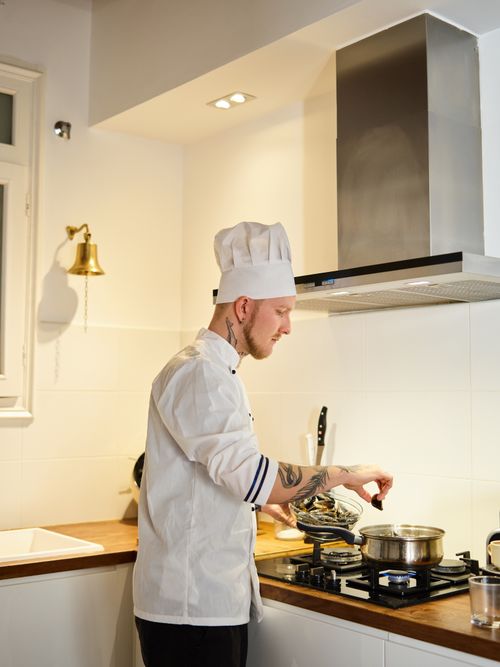 Free Side view of a male chef with tattoos cooking in a modern kitchen setting. Stock Photo
