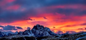 白雪皑皑的山脉上空，日落充满活力，映衬着鲜艳的天空