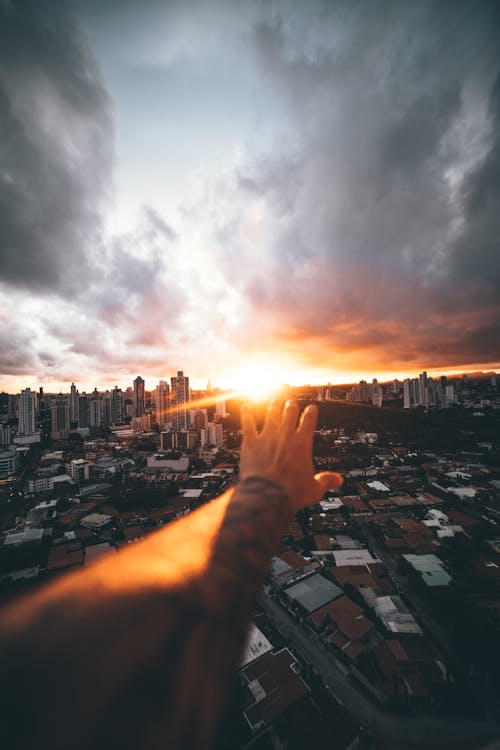 View of Cityscape at Sunset with Person's Hand Reaching Out 