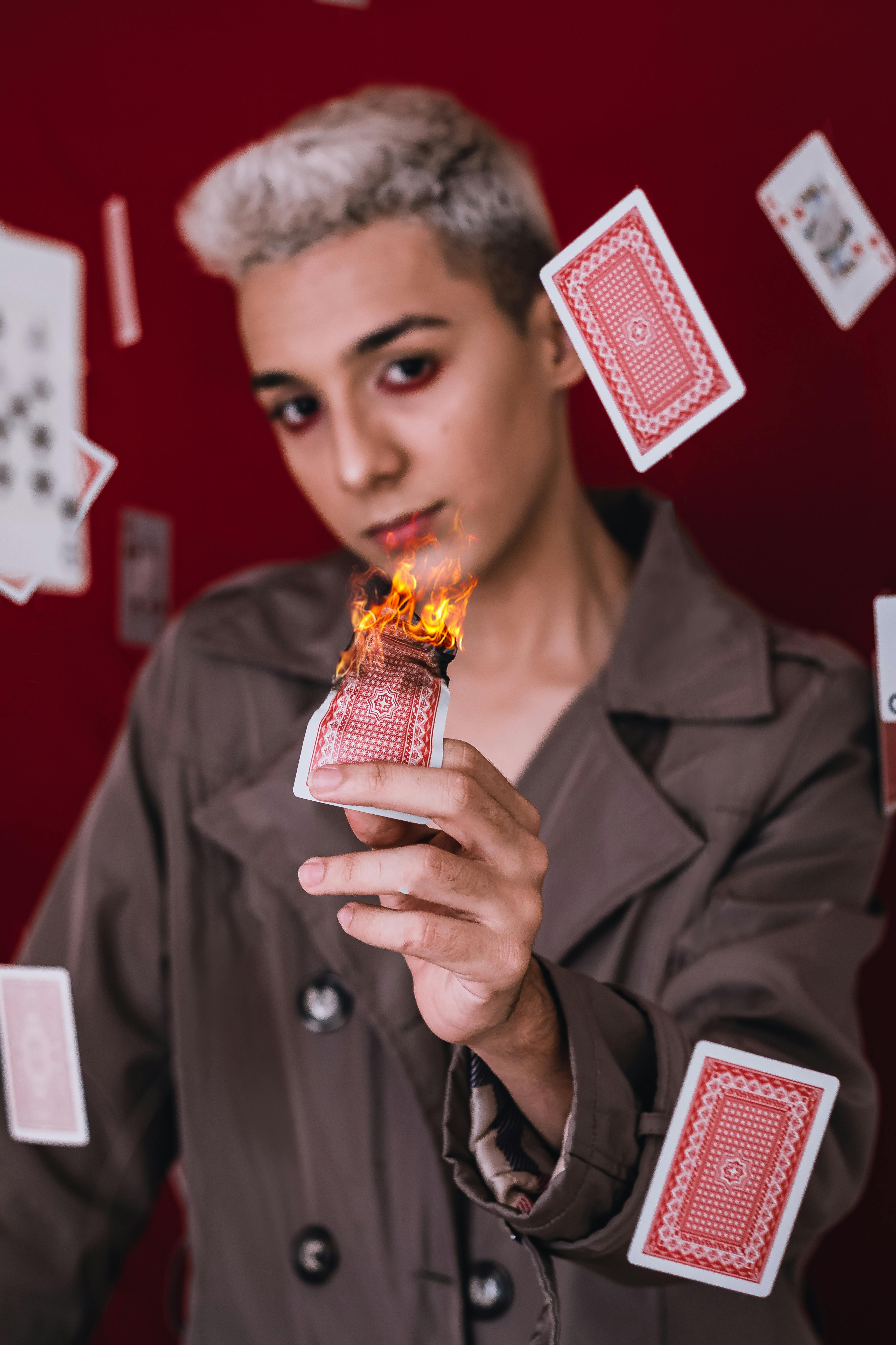 young man in brown coat holding a burning playing card