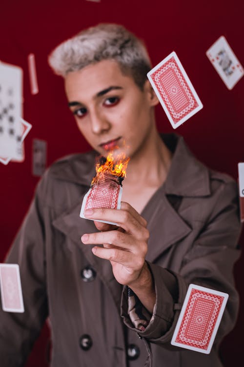 Free Young Man in Brown Coat Holding a Burning Playing Card Stock Photo
