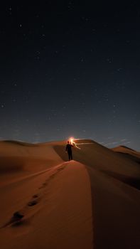 星空下，一个孤独的人影走过沙漠沙丘，光线指引着前路