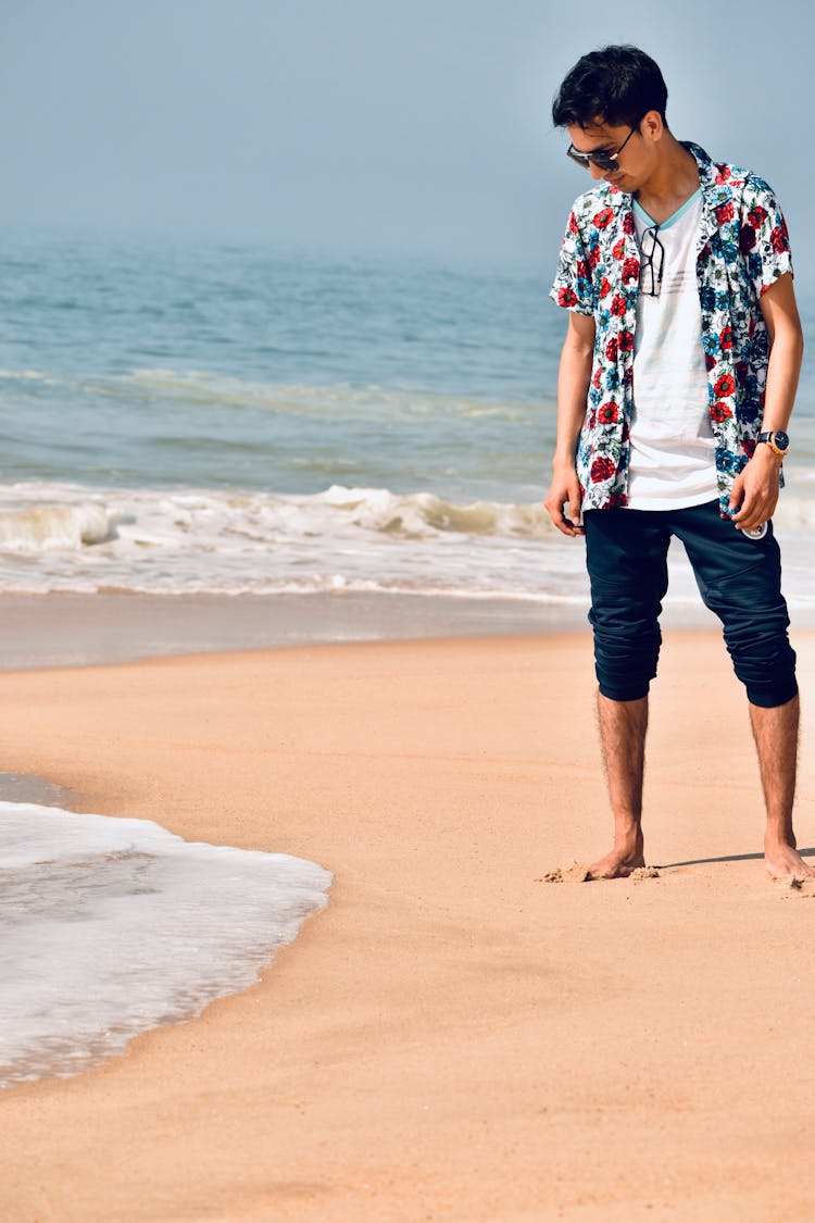 Man In Floral Button Up Shirt Standing On Beach Looking At The Wave