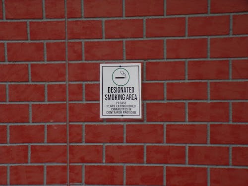 Building with brick wall and signboard with title indicating smoking area with symbol of cigarette