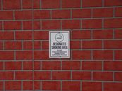 Building with brick wall and signboard with title indicating smoking area with symbol of cigarette