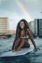 一位快乐的女子穿着泳衣，在沿海城市冲浪，身后有一道美丽的彩虹