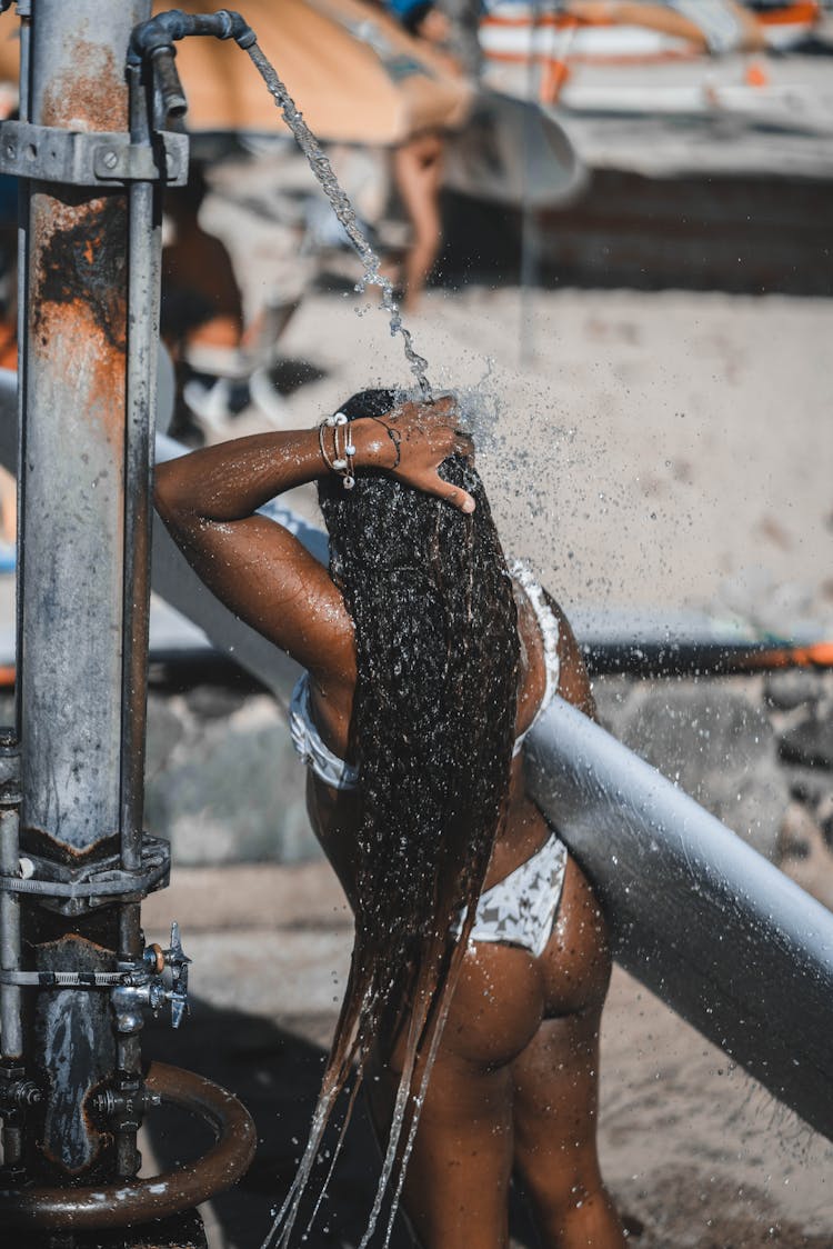 Back Of A Woman With Long Hair In A Bikini Under A Shower On A Beach