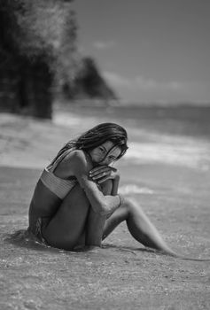 A young woman sits by the ocean, embracing tranquility on a beach in a stunning black and white portrait.