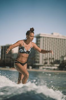 A woman skillfully surfs through crashing waves on a sunny tropical beach.