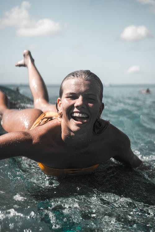 Free Woman in Yellow Bikini Smiling While Lying on Surfboard Stock Photo