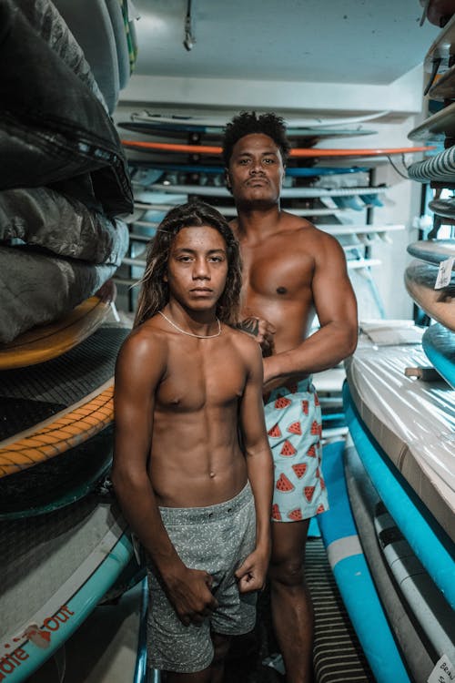 Topless Man and Teenage Boy Standing Between Surfboards in the Storage