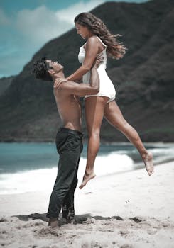 A joyful couple sharing a romantic moment on a scenic beach with mountains in the background.