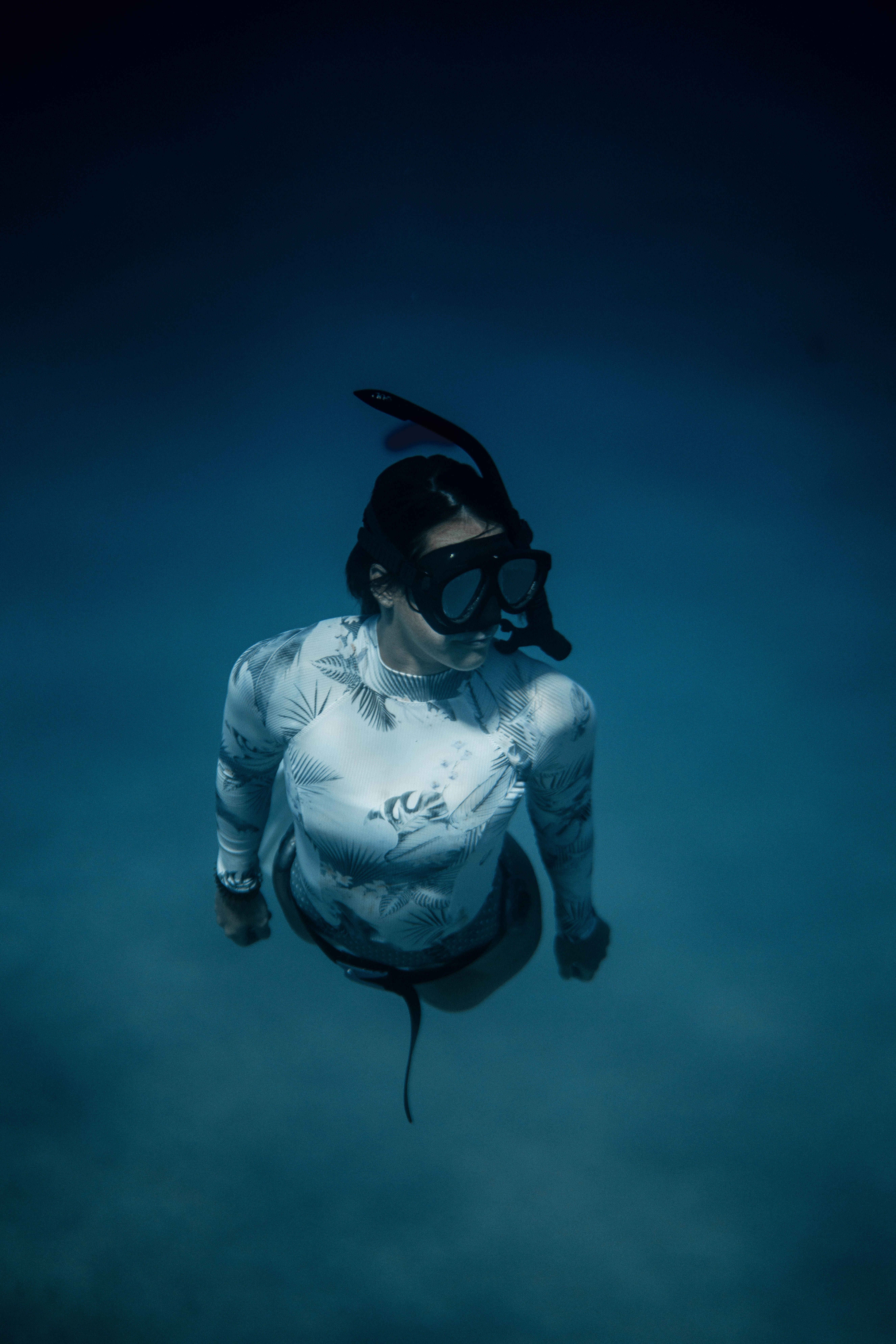 一名女子身着浮潜装备，在水下探索深蓝色的海洋，周围环绕着宁静的海洋生物
