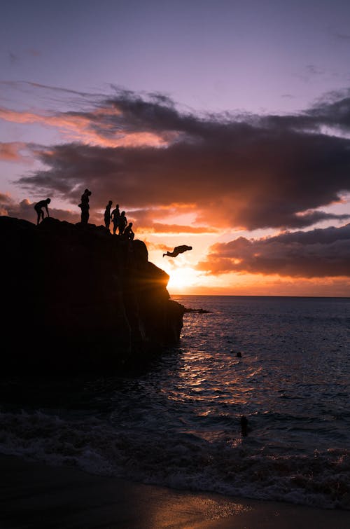 Silhouette of People Standing on Rock Formation Near Sea during Sunset
