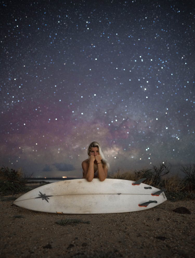 Woman Leaning On Surfboard Against Stars In Sky