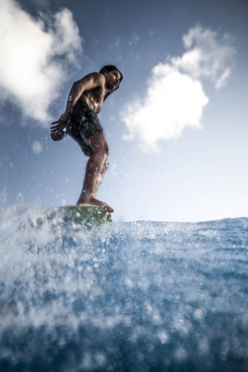 Free A surfer rides a wave with skill and balance under clear skies, captured in a dramatic low angle shot. Stock Photo