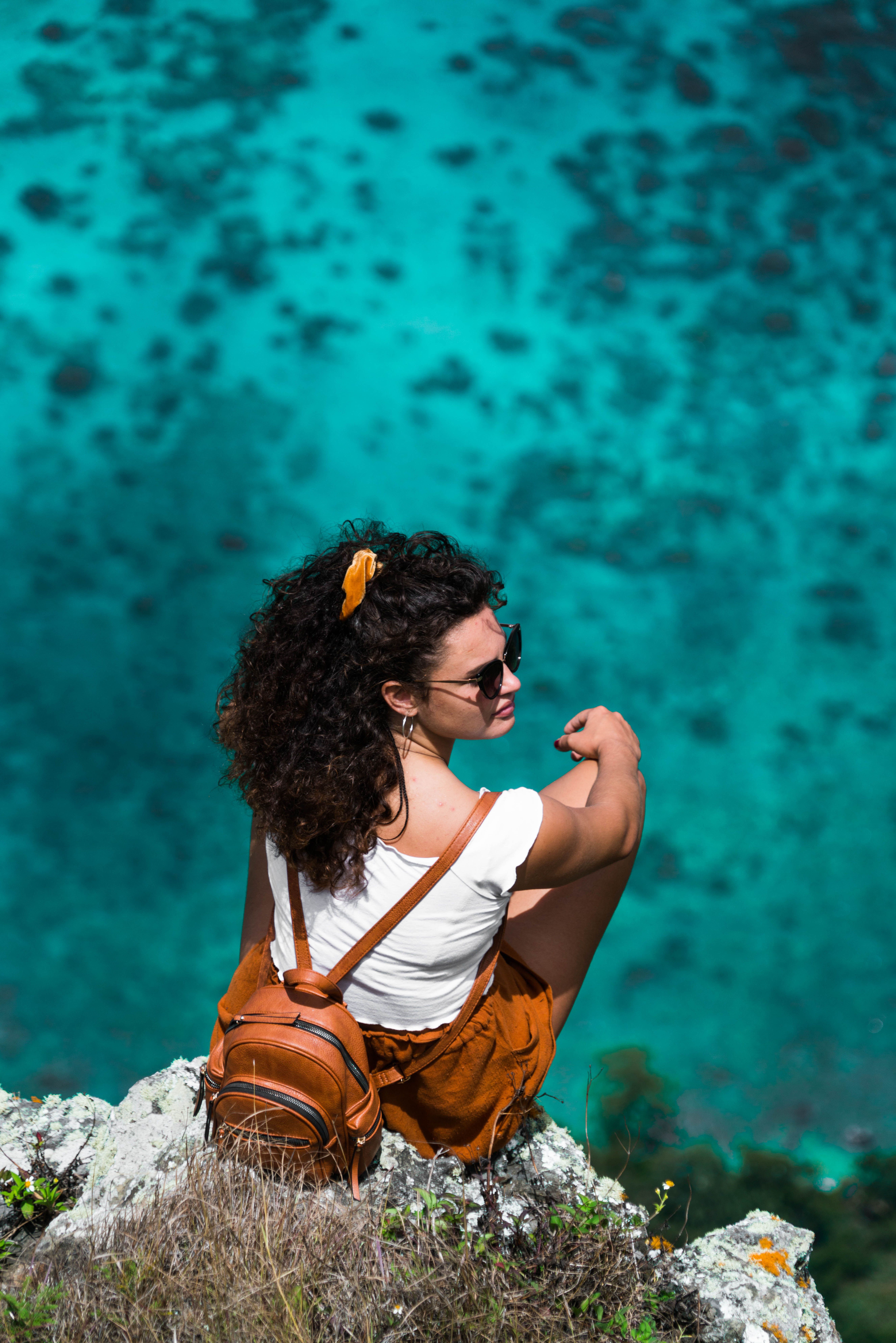 Woman in White Shirt and Brown Shorts Sitting on the Cliff · Free Stock ...
