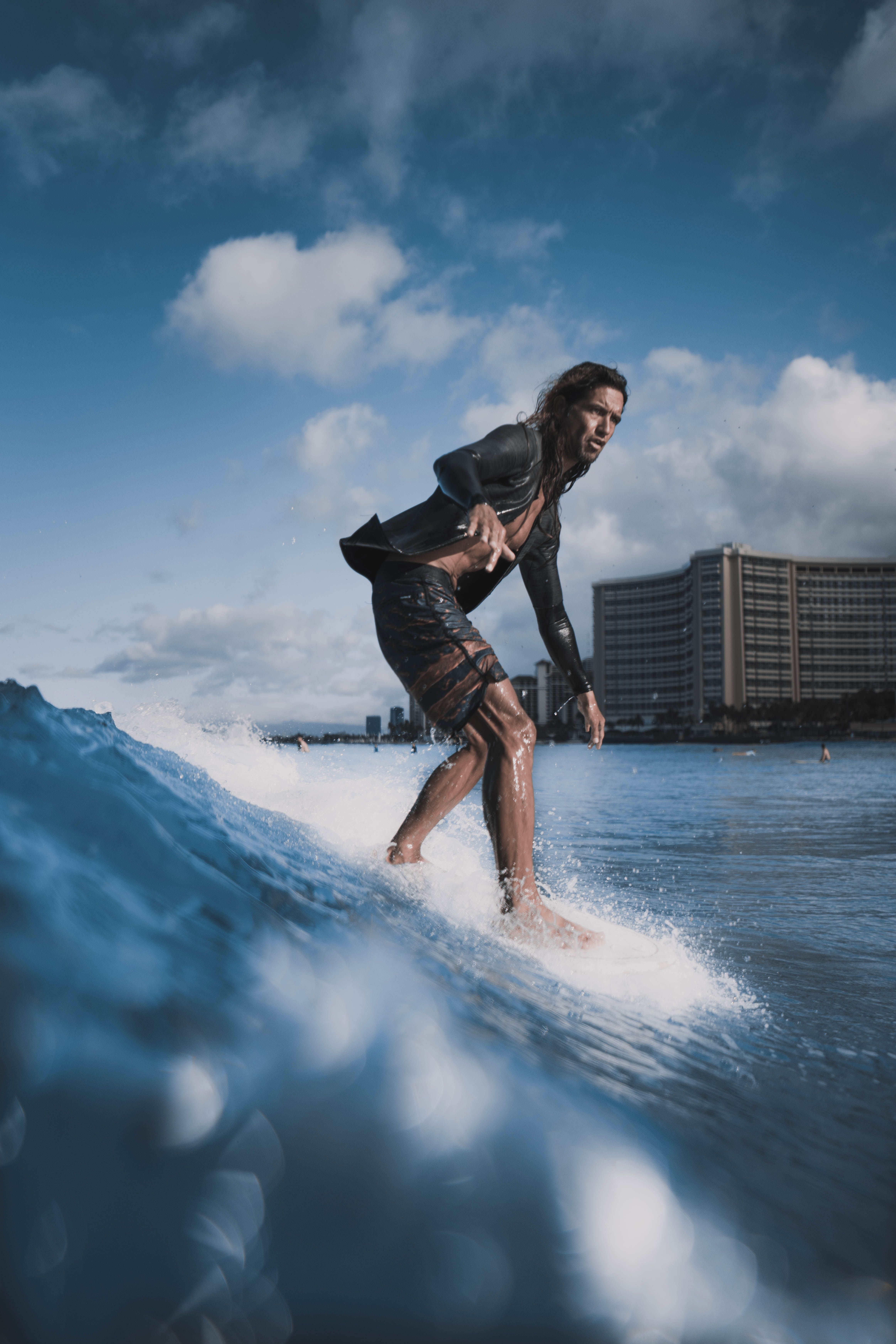 Action-packed shot of a surfer conquering a wave next to a coastal hotel under a clear blue sky.