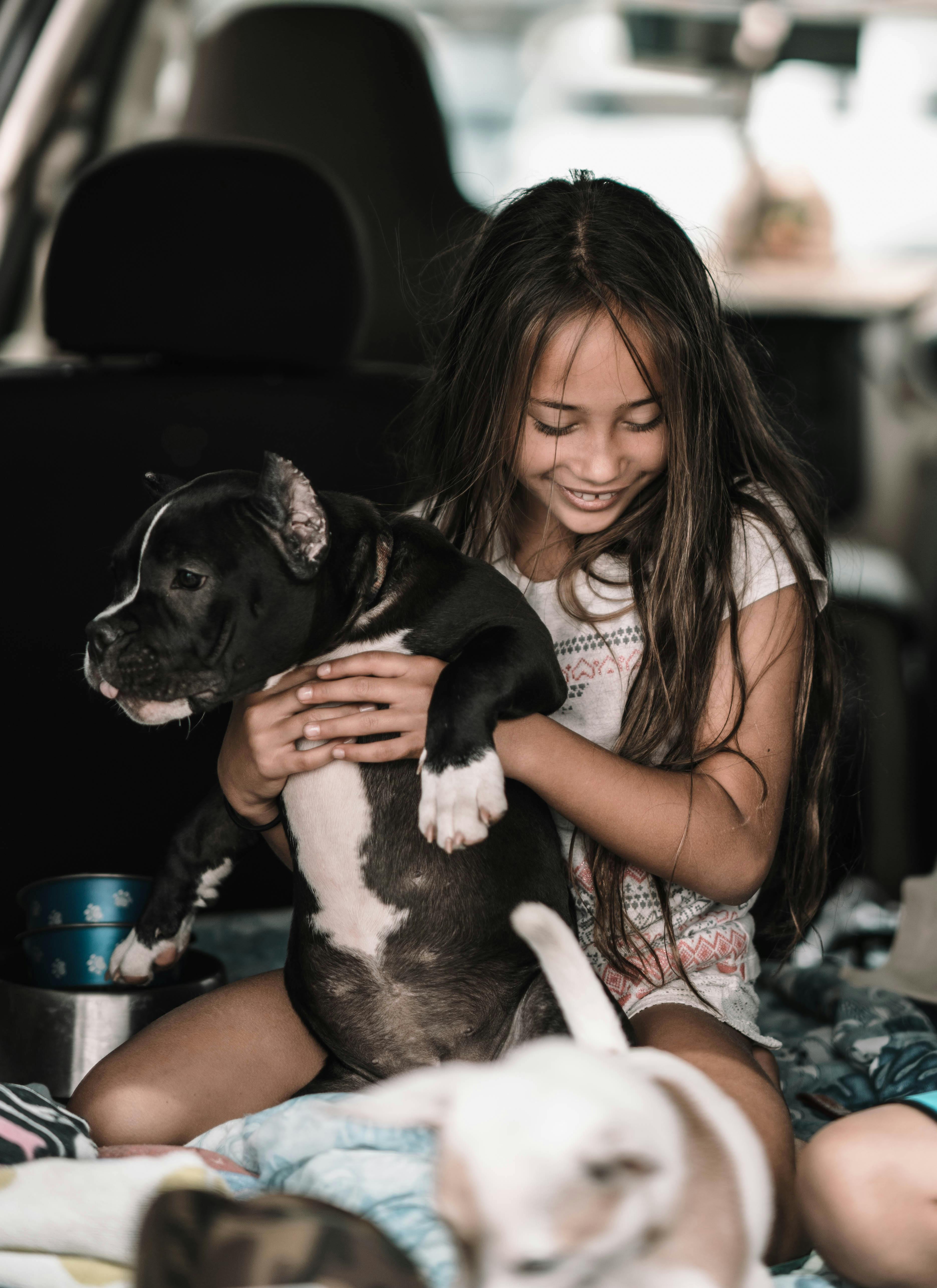 girl in white shirt carrying black and white dog