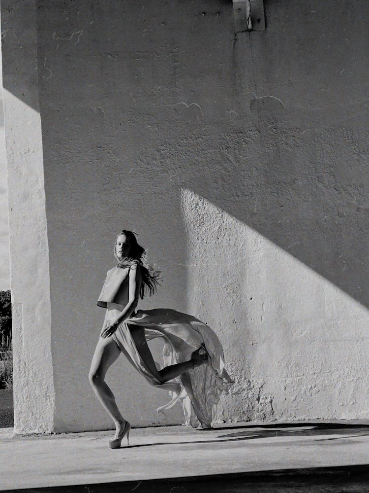 Woman In Long Skirt And High Heels Jumping Beside Wall