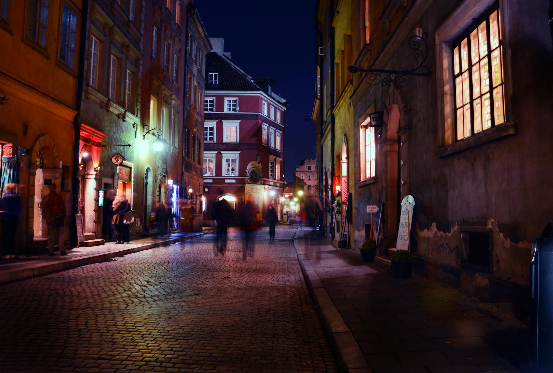 Charming night scene in a historic European city with blurred figures strolling under warm streetlights.