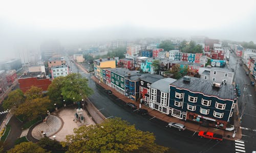 Drone view of colorful house facades near roadways with vehicles under white sky in foggy weather