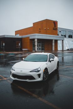 雨天，一辆时尚的白色跑车停在一栋现代建筑前的潮湿城区里